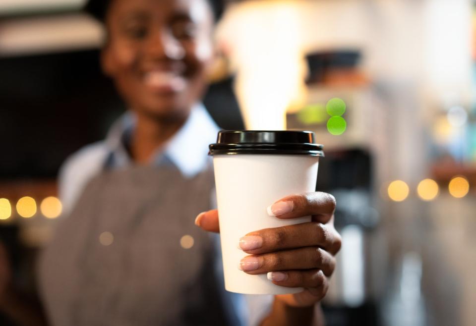 Barista holding out a coffee cup.